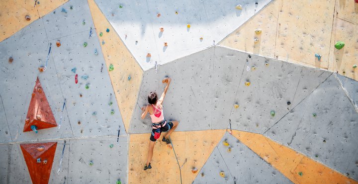 Sportswoman climber moving up on steep rock, climbing on artificial wall. Extreme sports and bouldering concept